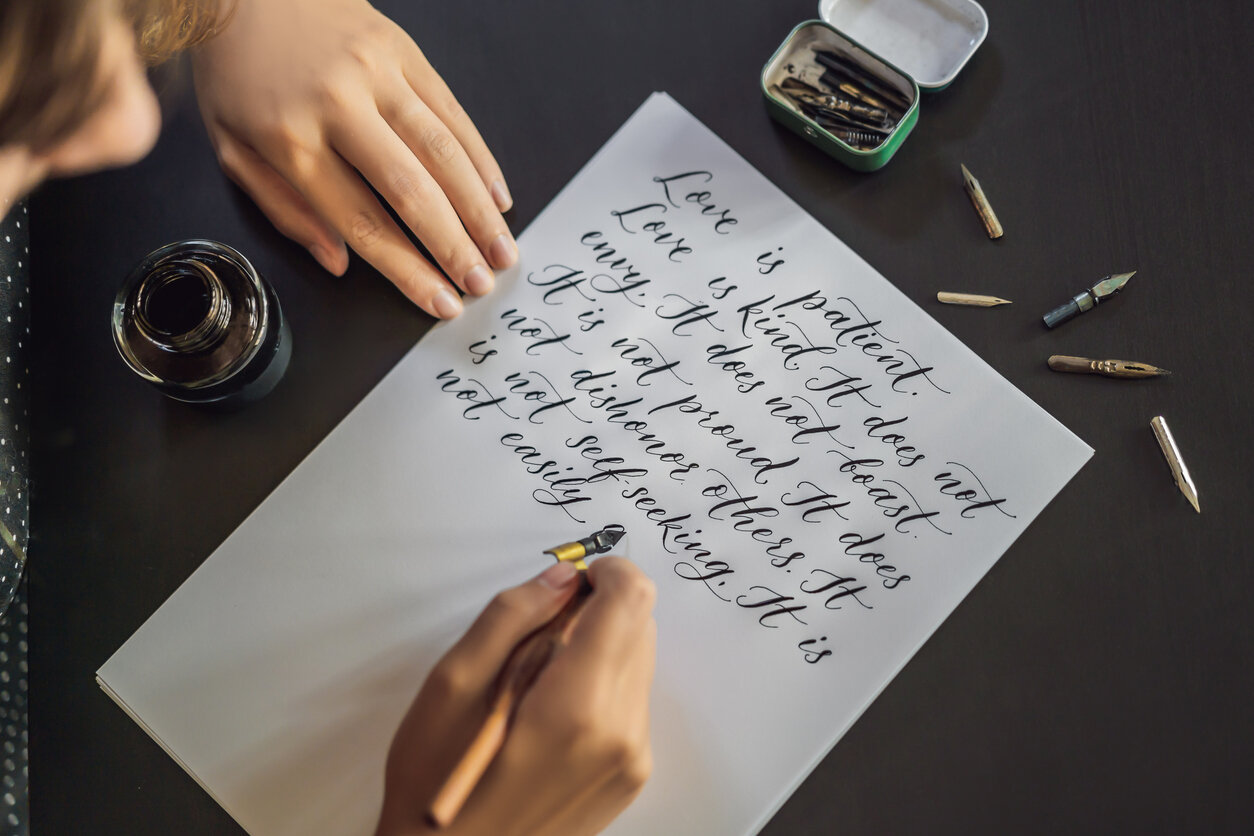 Hand, die eine Kalligrafiefeder hält und auf ein Stückpapier schreibt. 