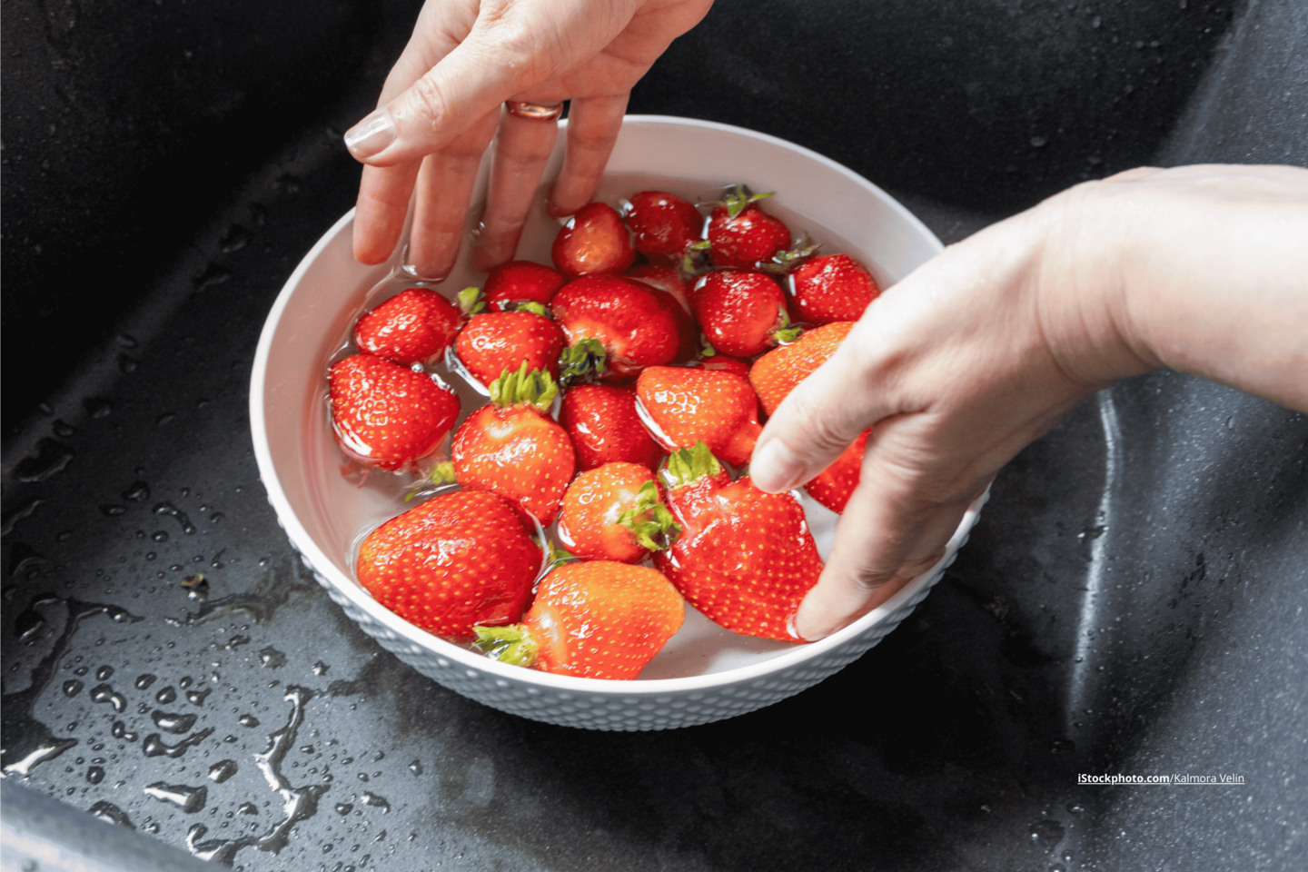Eine Schüssel, in der Erdbeeren im Wasser liegen und Hände, die in die Schüssel greifen. 