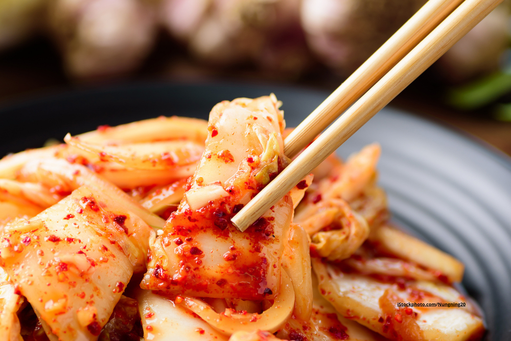 Ein Teller, auf dem Kimchi liegt und Stäbchen, die ein Stück Kimchi halten. 