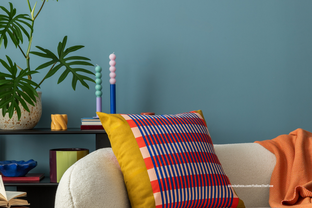 Ein Sofa mit bunten Kissen und weitere farbenfrohe Dekoelemente. Die Wand ist blau. 