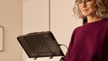 Eine ältere Frau, die in einer Küche steht und ein iPad mit optaro® XL nutzt.