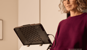 Eine ältere Frau, die in einer Küche steht und ein iPad mit optaro® XL nutzt.