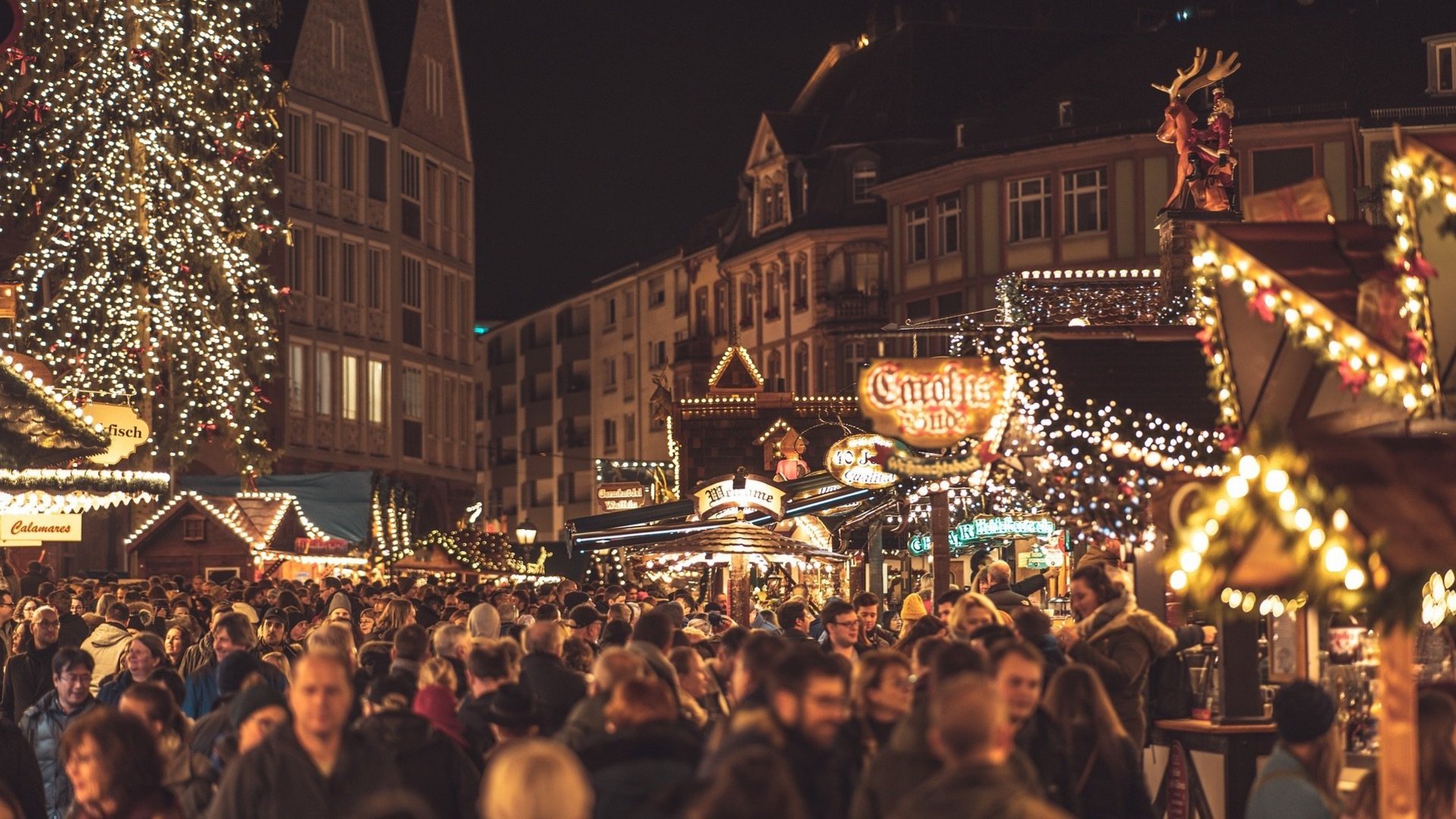 Das Bild zeigt eine Menschenmenge auf einem beleuchteten Weihnachtsmarkt.