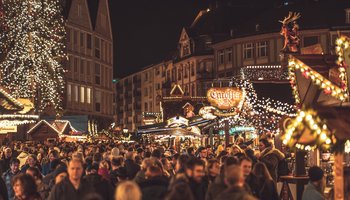 Das Bild zeigt eine Menschenmenge auf einem beleuchteten Weihnachtsmarkt.