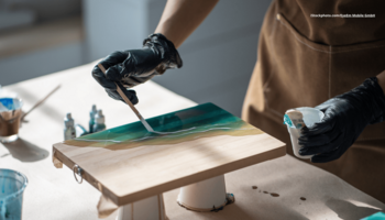 Das Foto zeigt die Hände einer Person, die auf Holz ein Kunstwerk aus Resin schafft.