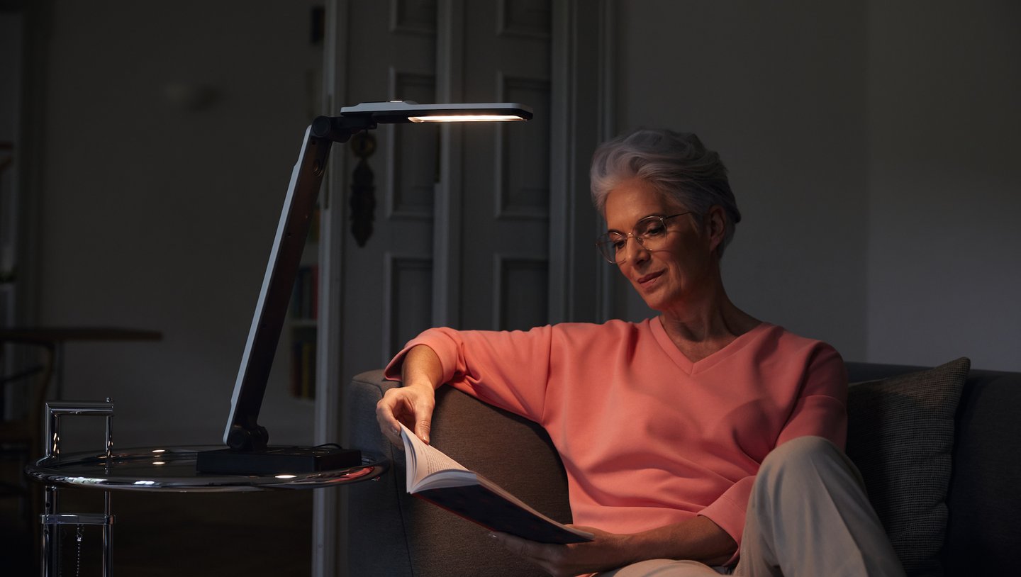 Das Foto zeigt eine Frau, die ein Buch unter der Tischleuchte elumentis LED liest. 