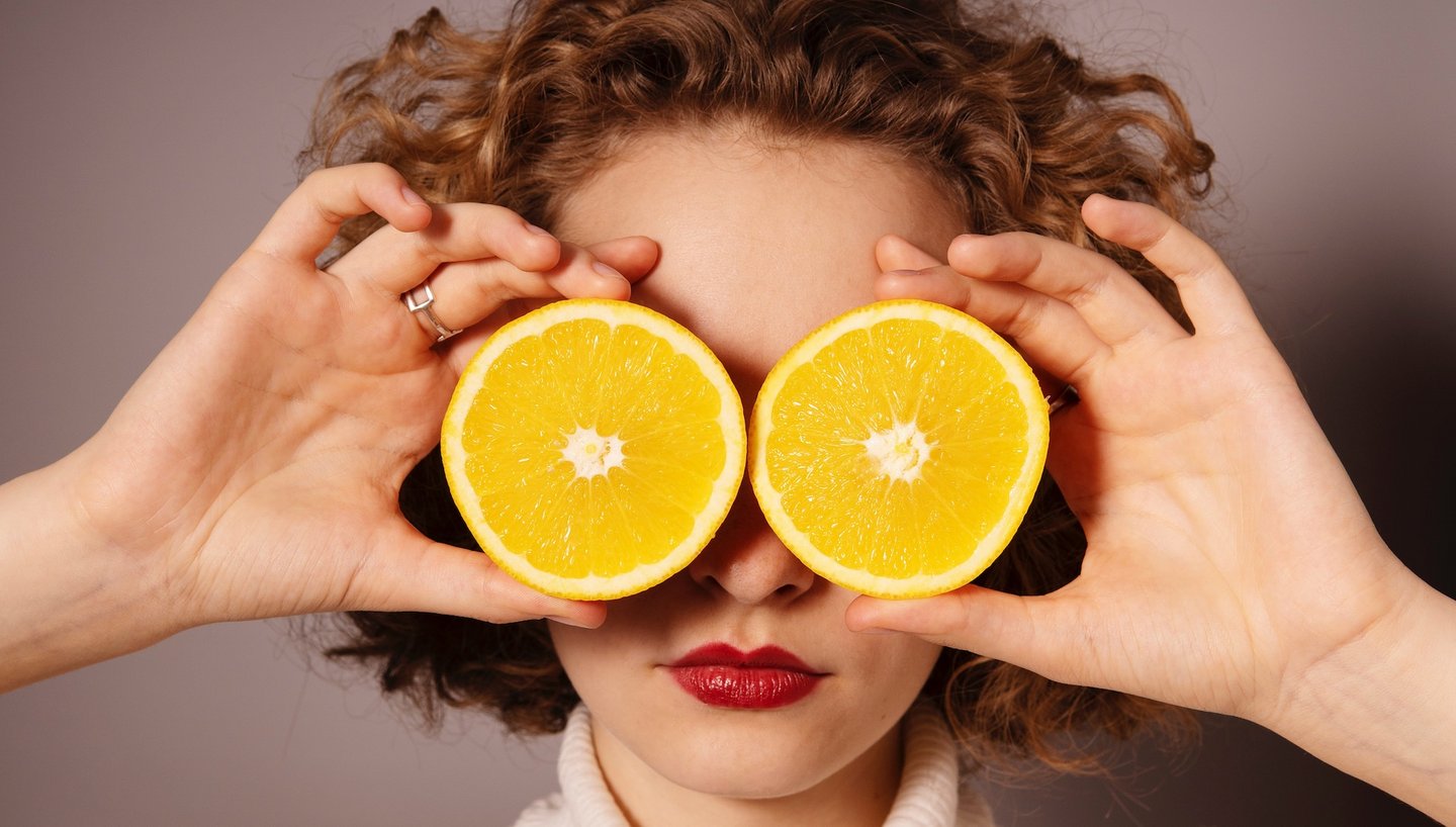 Auf diesem Bild hält eine Frau zwei Orangenhälften vor ihren Augen.