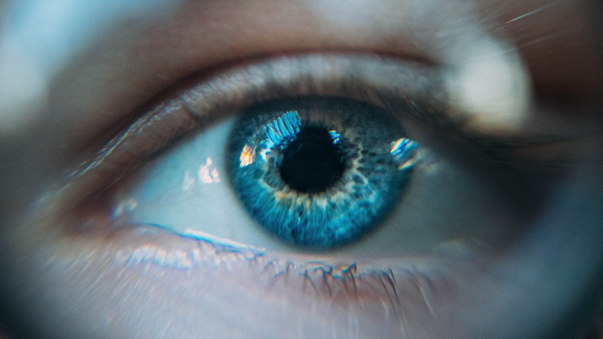 Das Bild zeigt ein blaues Auge vor einem verschwommenen Filter.