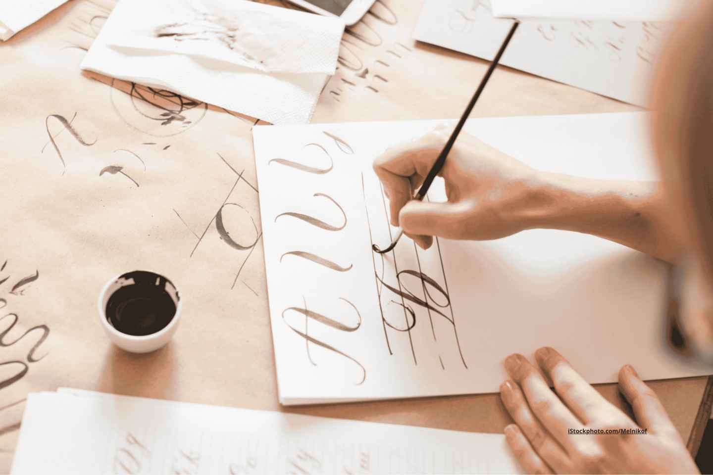 Hände, die eine Kalligrafie-Übung mit einer Feder auf einem weißen Blatt Papier machen.