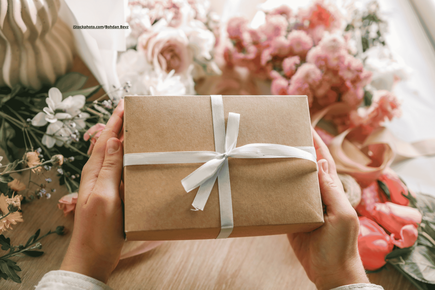 Geschenkbox wird von Händen gehalten. Darum herum liegen Blumen.