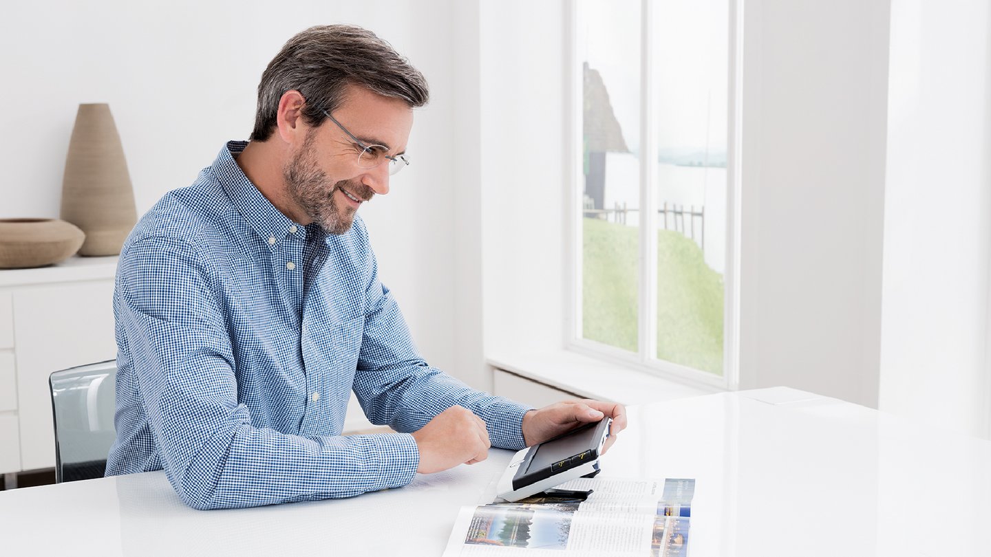 Das Foto zeigt einen Mann mit der elektronischen Sehhilfe visolux DIGITAL von Eschenbach Optik.vis