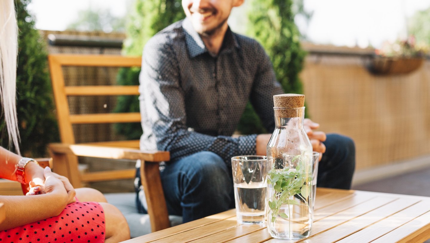 Das Bild zeigt zwei Personen, welche auf dem Balkon sitzen und Wasser trinken.