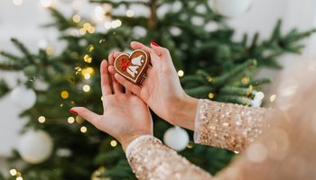 Ein Lebkuchenherz wird vor einen Weihnachtsbaum gehalten.