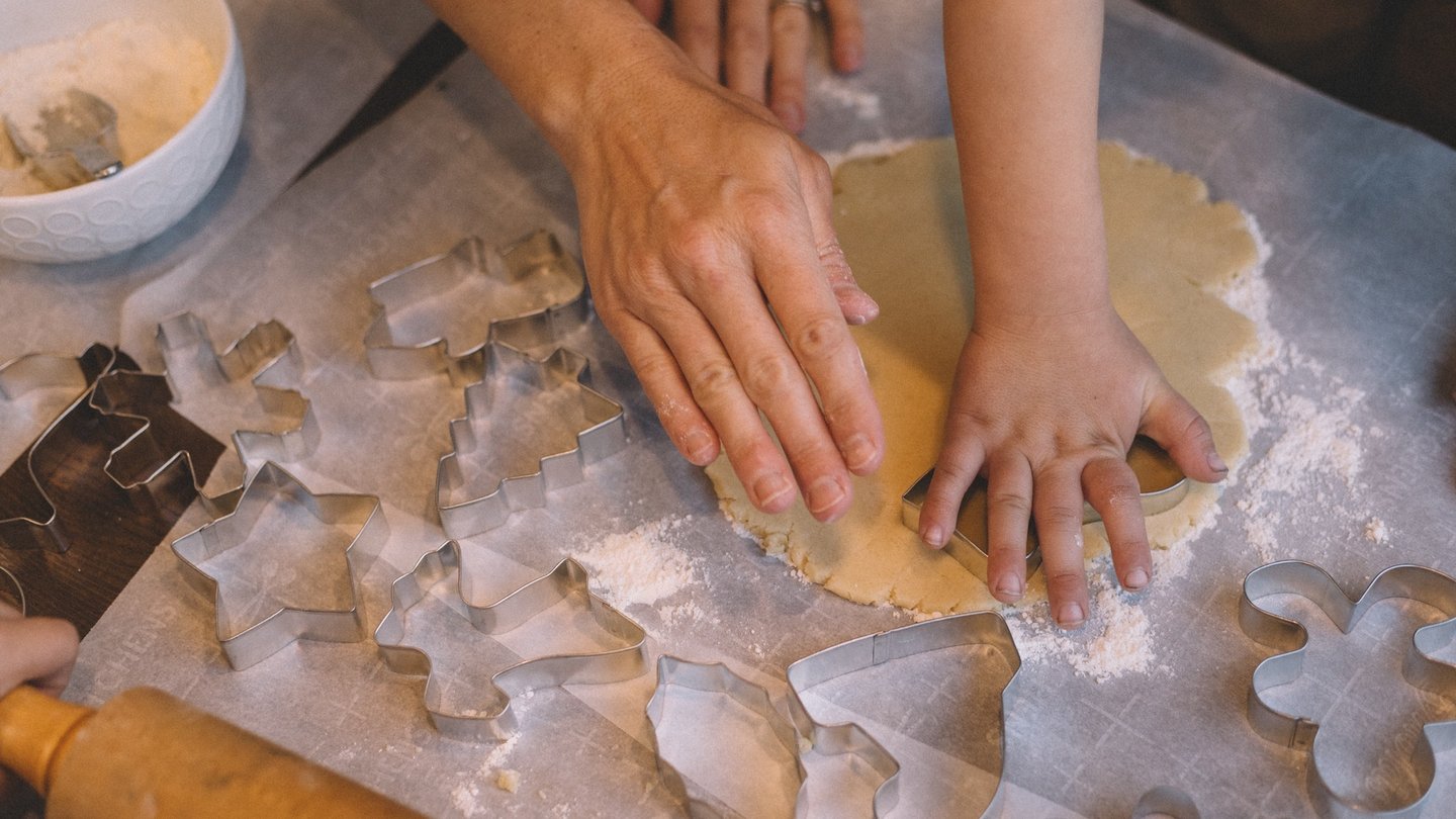 Das Foto zeigt die Hände eines Kindes und Erwachsenen, die Plätzchen ausstechen.