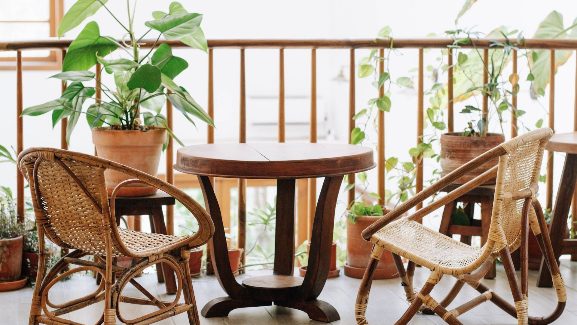 Das Bild zeigt einen Balkon mit einem Tisch, Stühlen und grünen Pflanzen.