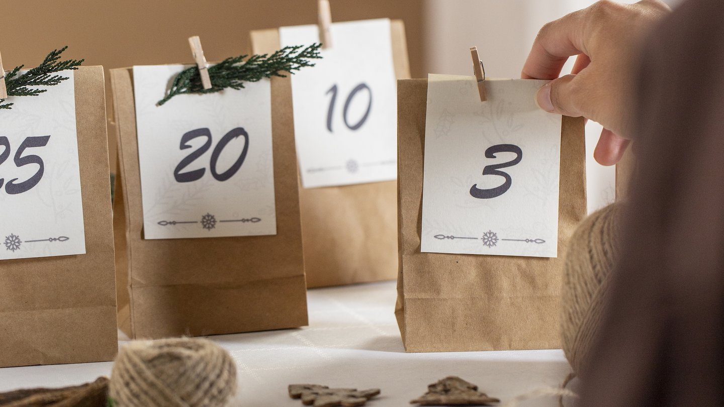 Das Foto zeigt eine Person, die einen Adventskalender aus Papiertüten selbst bastelt.