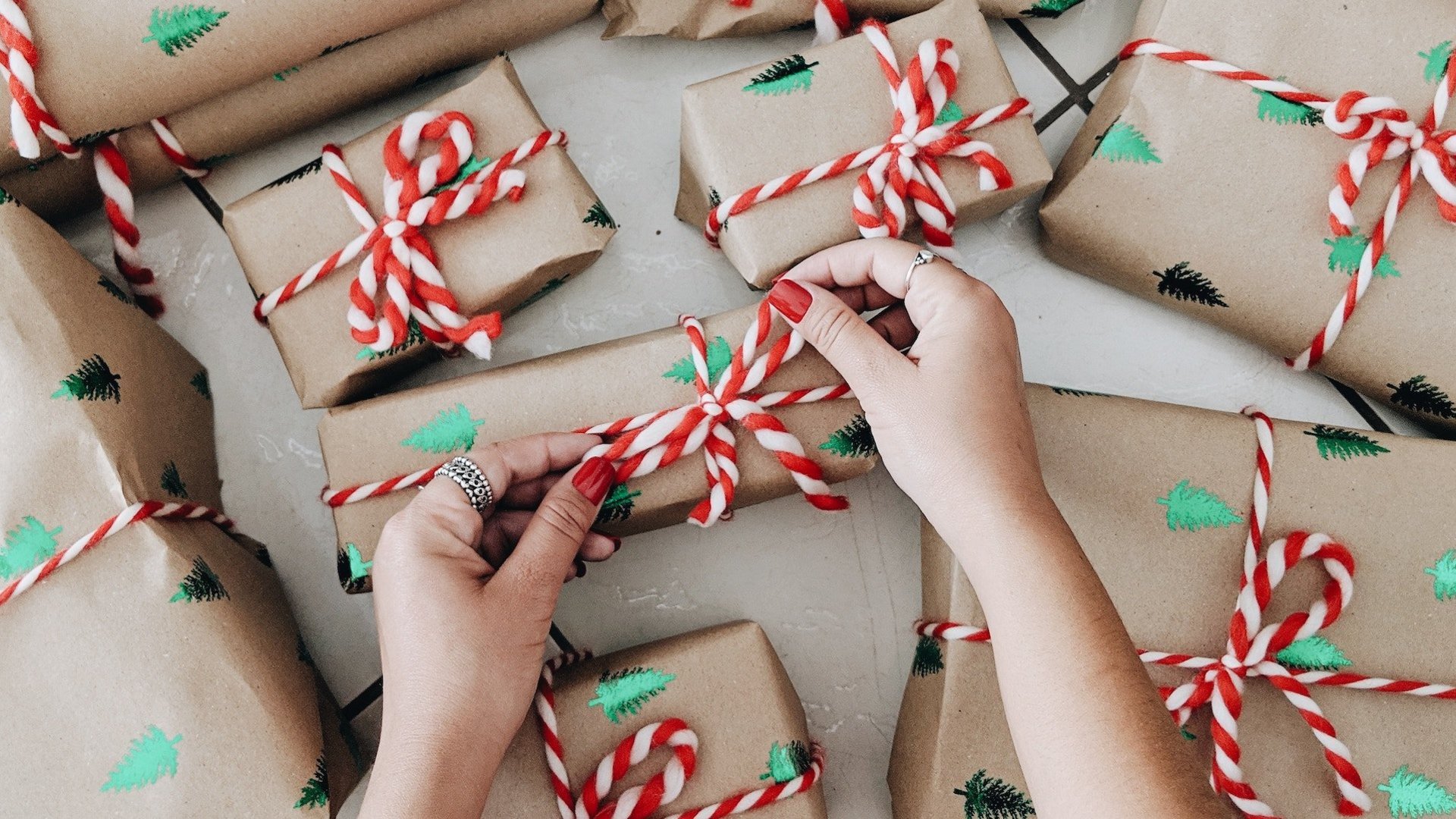 Das Foto zeigt zwei Hände, die eine Schleife an ein Weihnachtsgeschenk binden.
