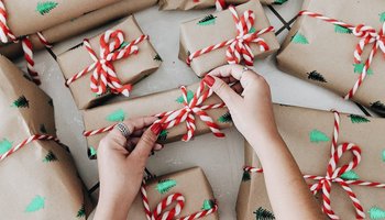 Das Foto zeigt zwei Hände, die eine Schleife an ein Weihnachtsgeschenk binden.