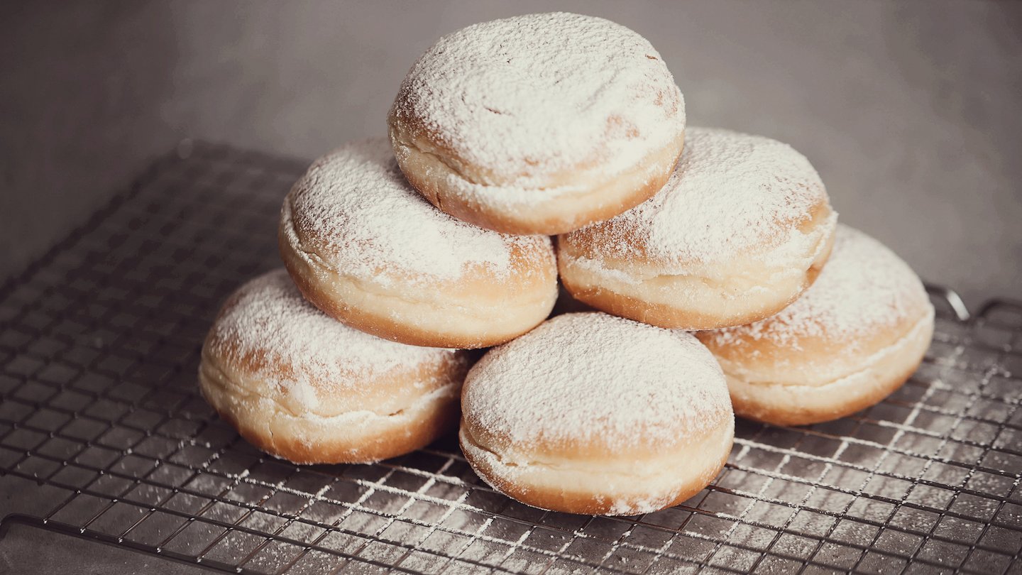 Das Foto zeigt Berliner mit Puderzucker auf einem Abtropfgitter.