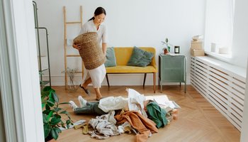 Eine Frau trägt einen Korb zu einem Wäschehaufen auf dem Boden.
