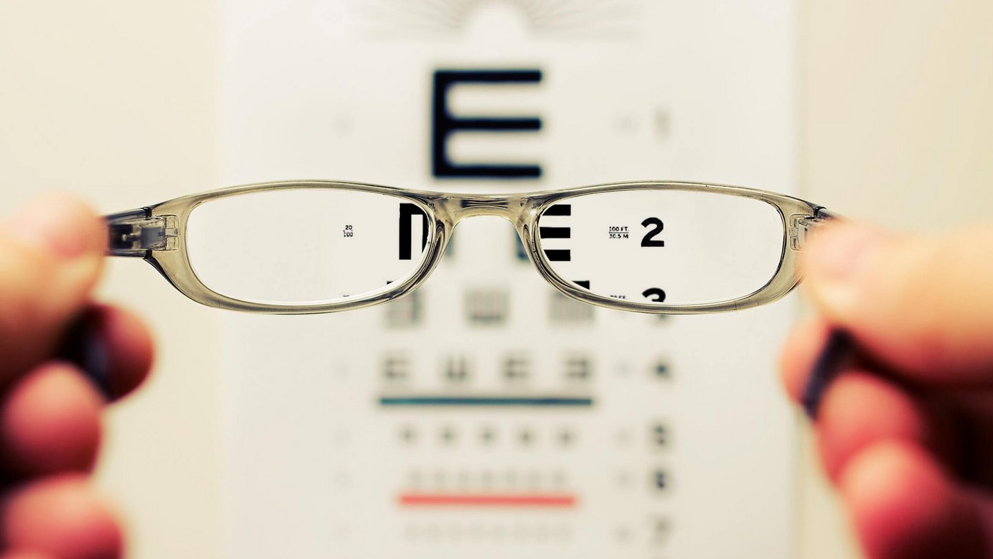 Eine Brille und eine verschwommene Buchstabentafel für einen Sehtest werden abgebildet.