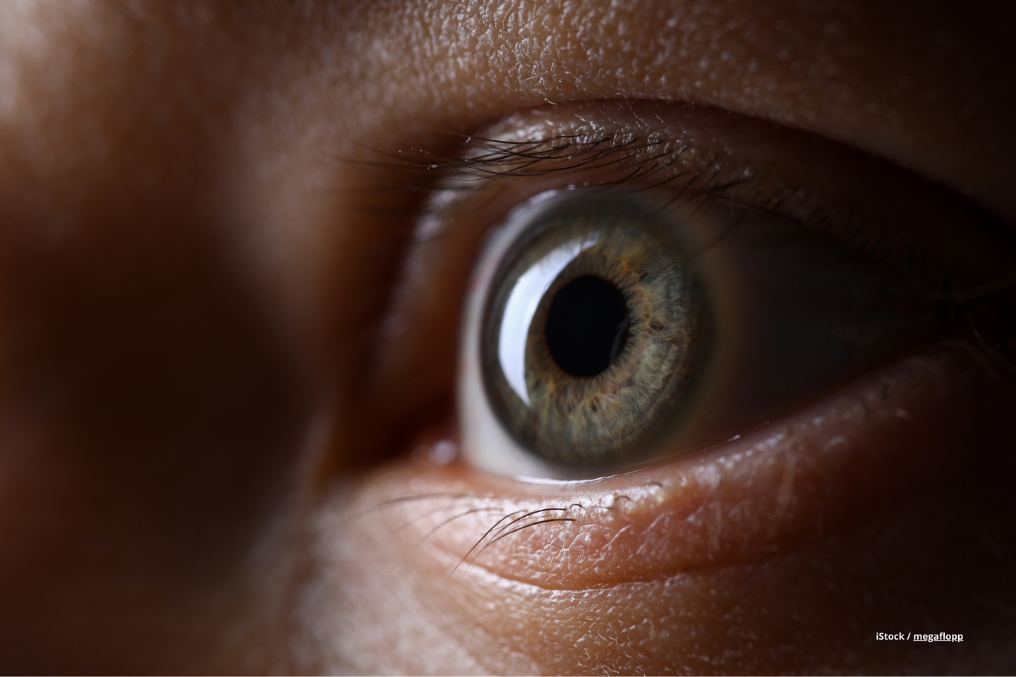 Das Bild zeigt ein blaues Auge vor einem dunklen Hintergrund.