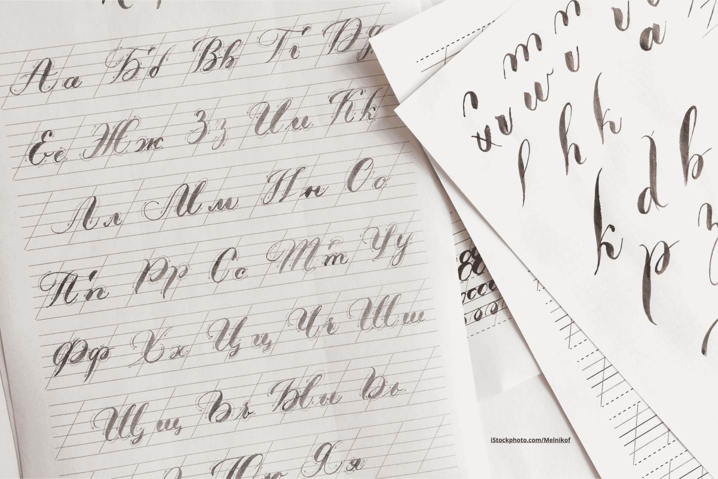 Mehrere Bögen Kalligraphie-Papier, die übereinander liegen, beschrieben mit verschiedenen Buchstaben.