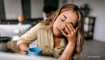 Das Foto zeigt eine müde Frau am Schreibtisch, die ihre Hand vor die Augen hält.