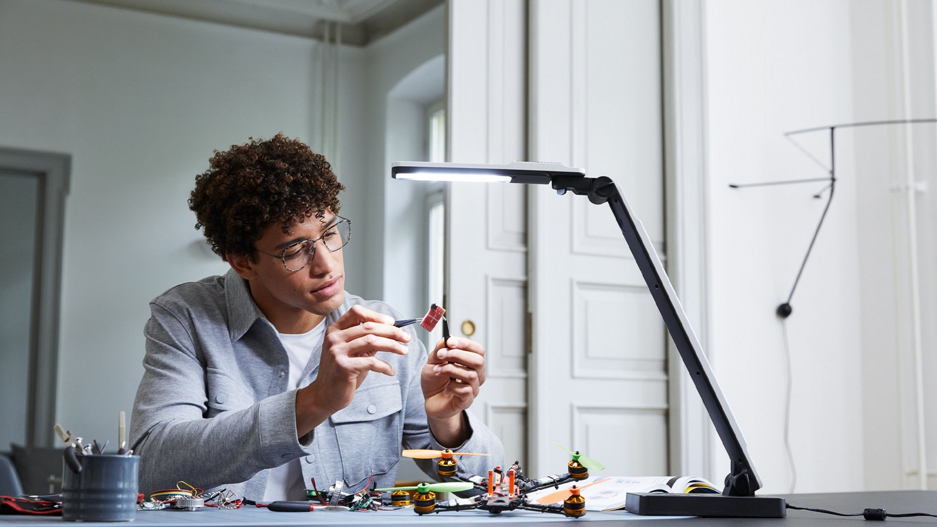 Ein Mann macht Bastelarbeiten an einem Schreibtisch unter der Leuchtlampe elumentis LED.