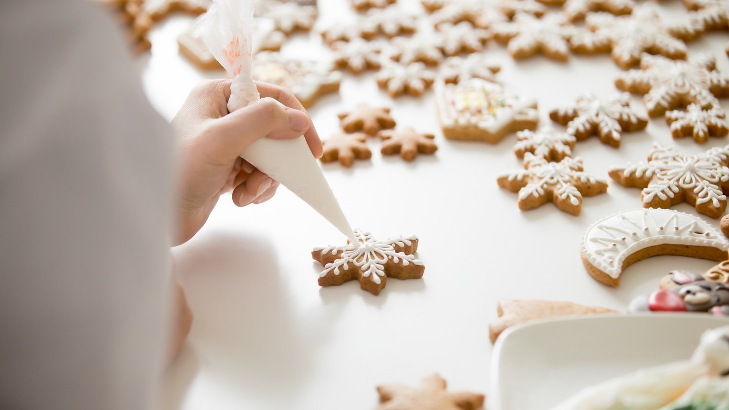 Das Foto zeigt eine Person, die Plätzchen mit einem Spritzbeutel und Zuckerguss dekoriert.