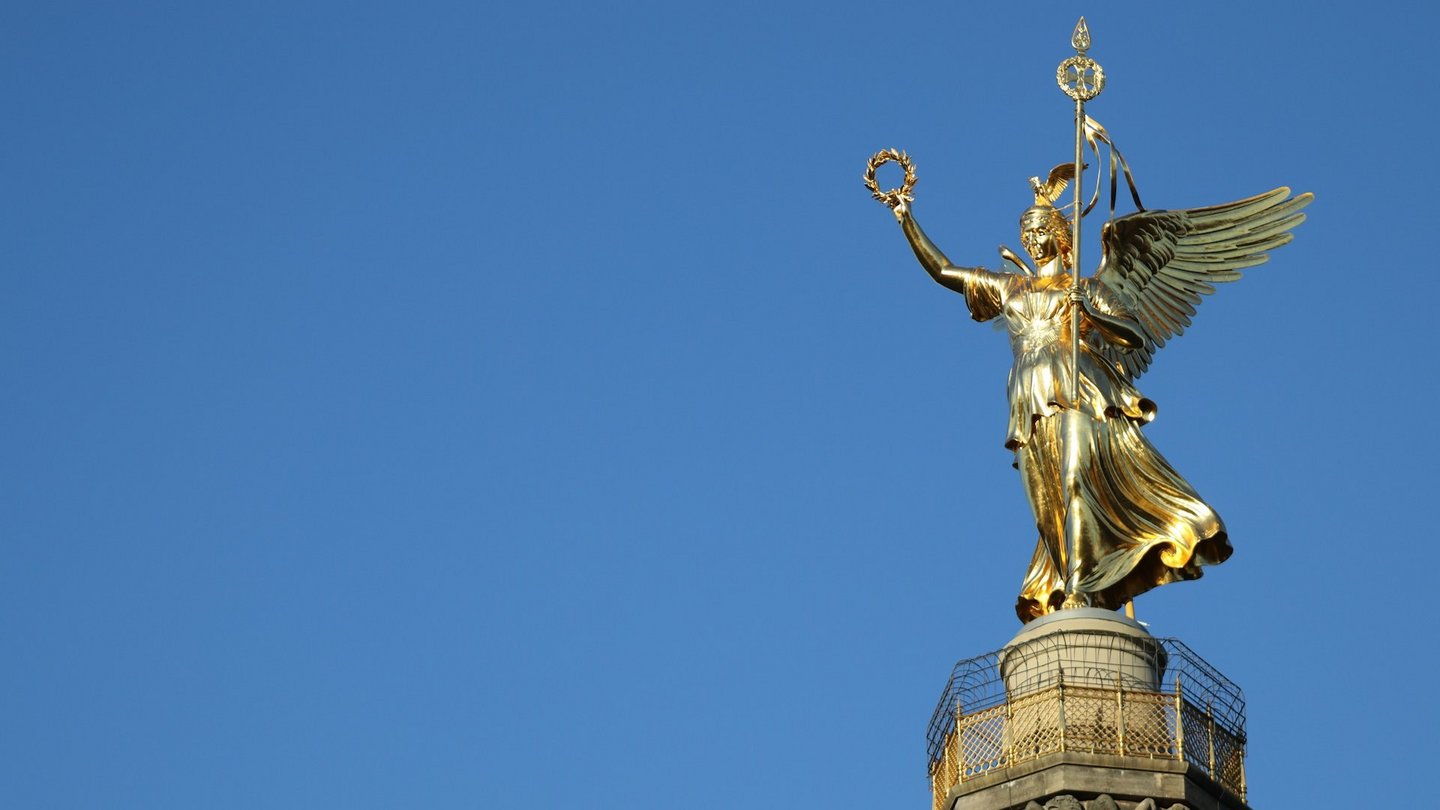 Die Siegessäule in Berlin mit der goldenen Viktoria-Statue, die stolz in den klaren blauen Himmel ragt.
