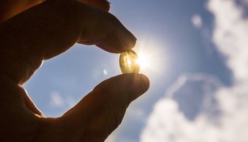 Das Foto zeigt eine Hand, die eine Vitamin-D-Tablette vor blauem Himmel gegen die Sonne hält.