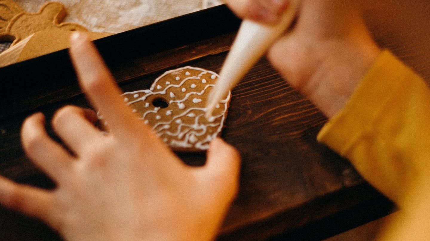 Ein Lebkuchenherz wird mit Zuckerguss aus einer Spritztülle verziert.