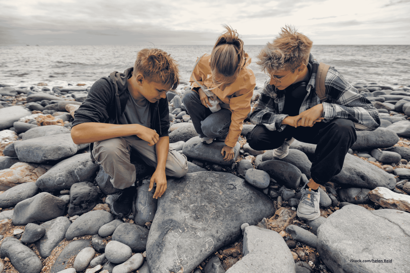 Das Foto zeigt eine Familie am Meer an einem Steinstrand beim Entdecken von Fossilien.