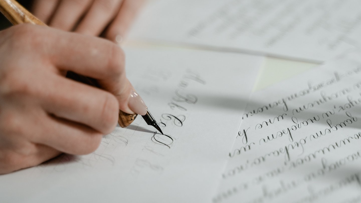 Das Bild zeigt eine Person, die mit einem Federhalter schreibt.