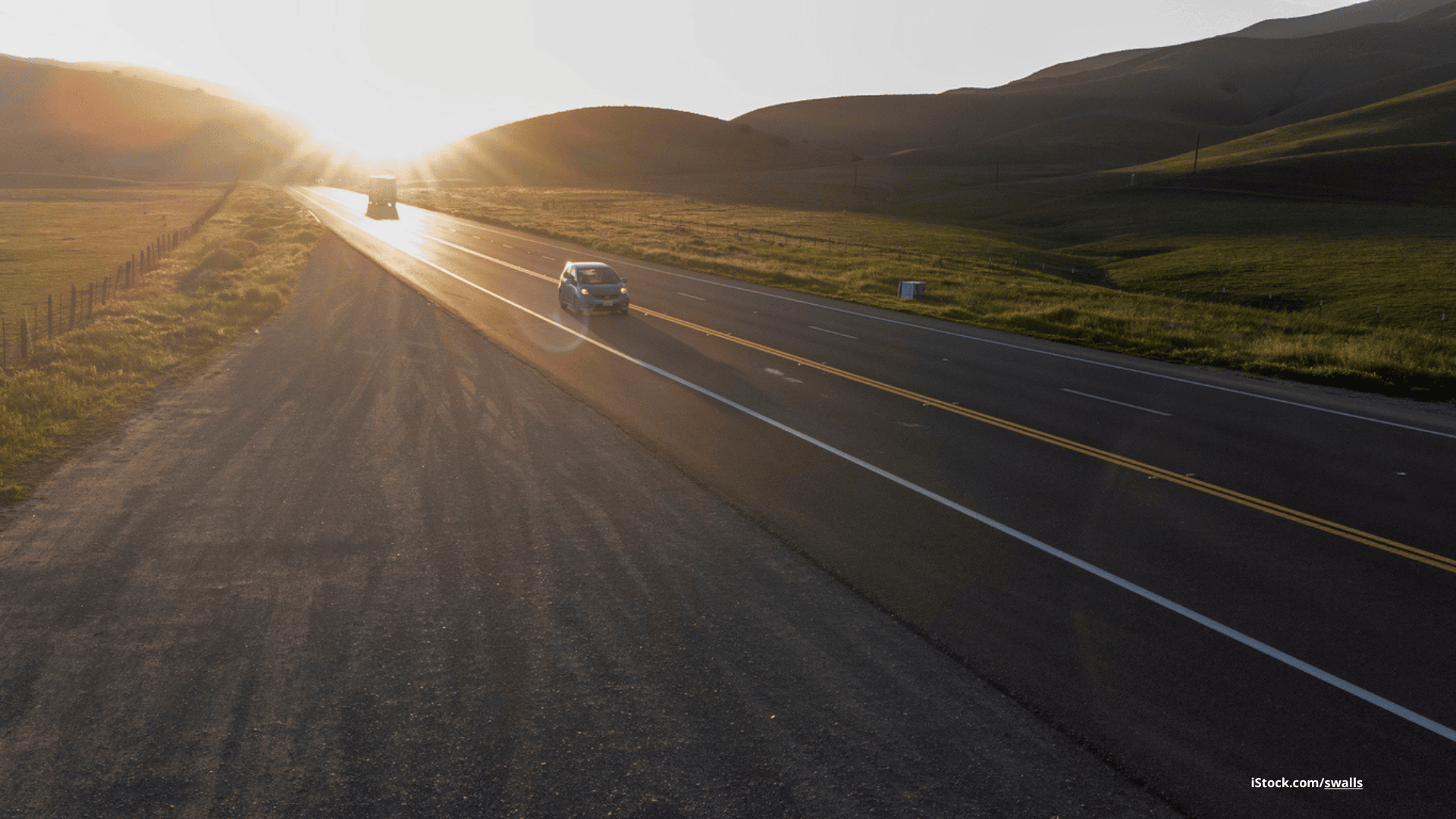 Das Foto zeigt eine Landstraße, auf der zwei Autos bei tief stehender Sonne fahren.
