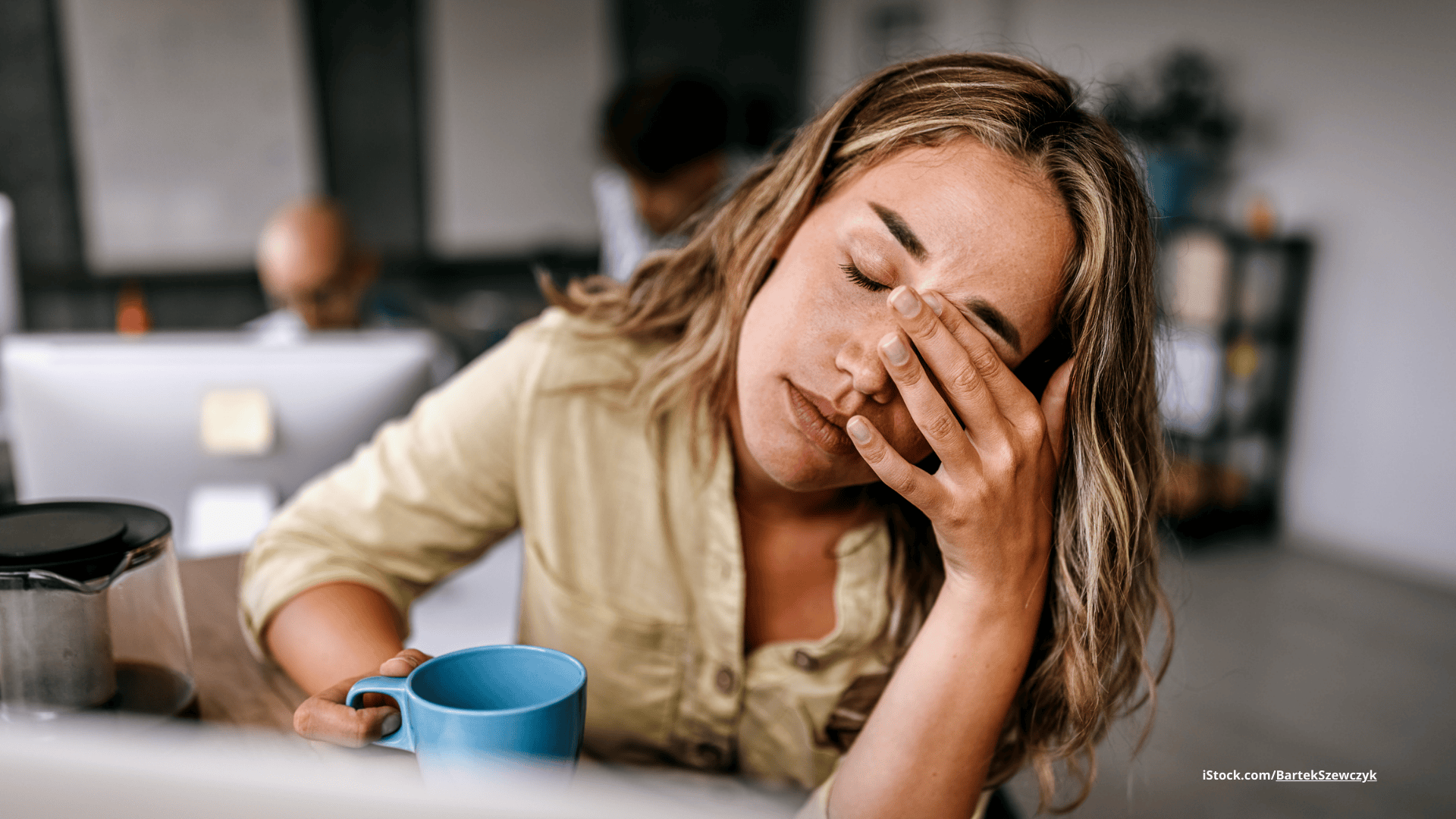 Das Foto zeigt eine müde Frau am Schreibtisch, die ihre Hand vor die Augen hält.